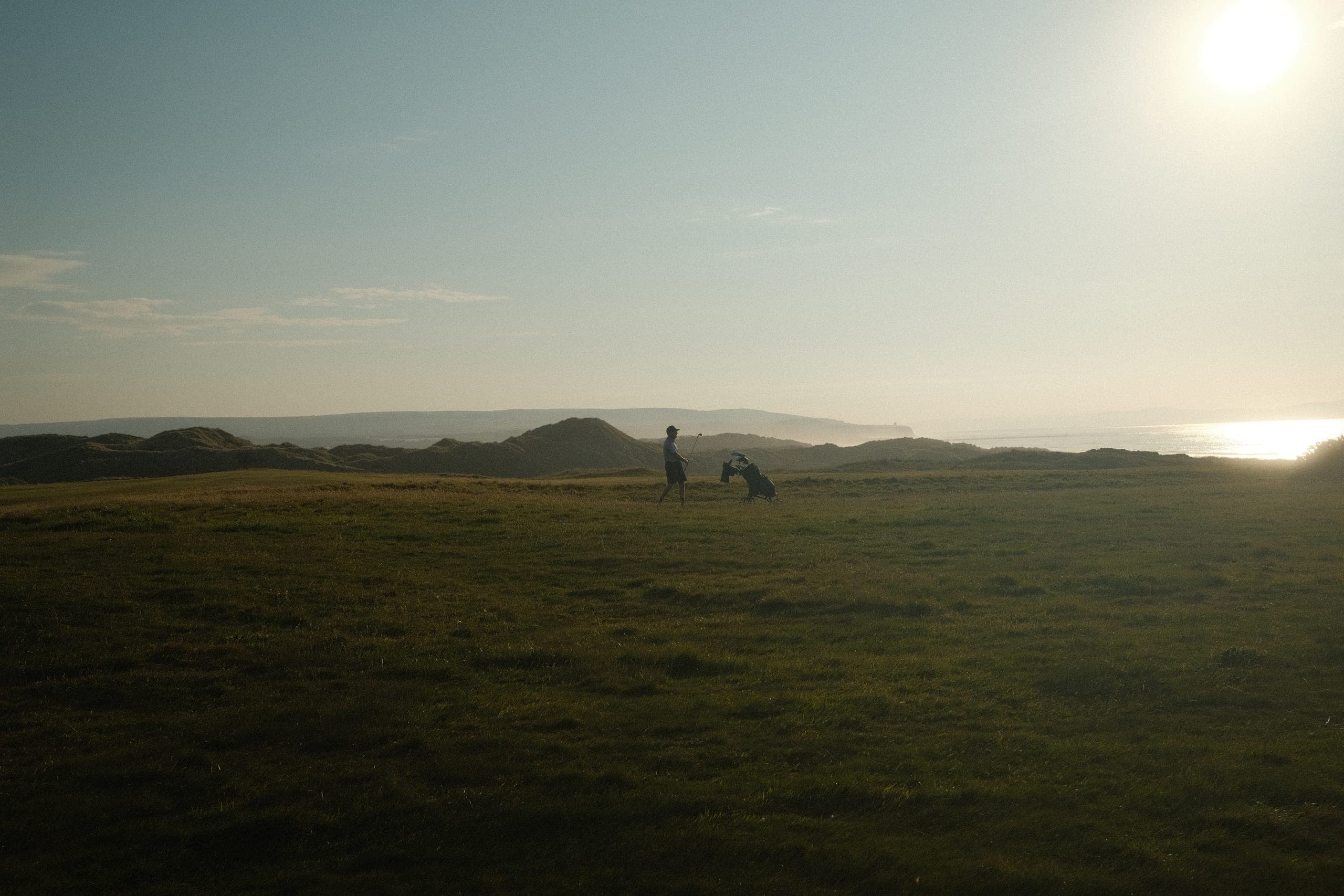 A lone golfer walking with a bag into low sun.