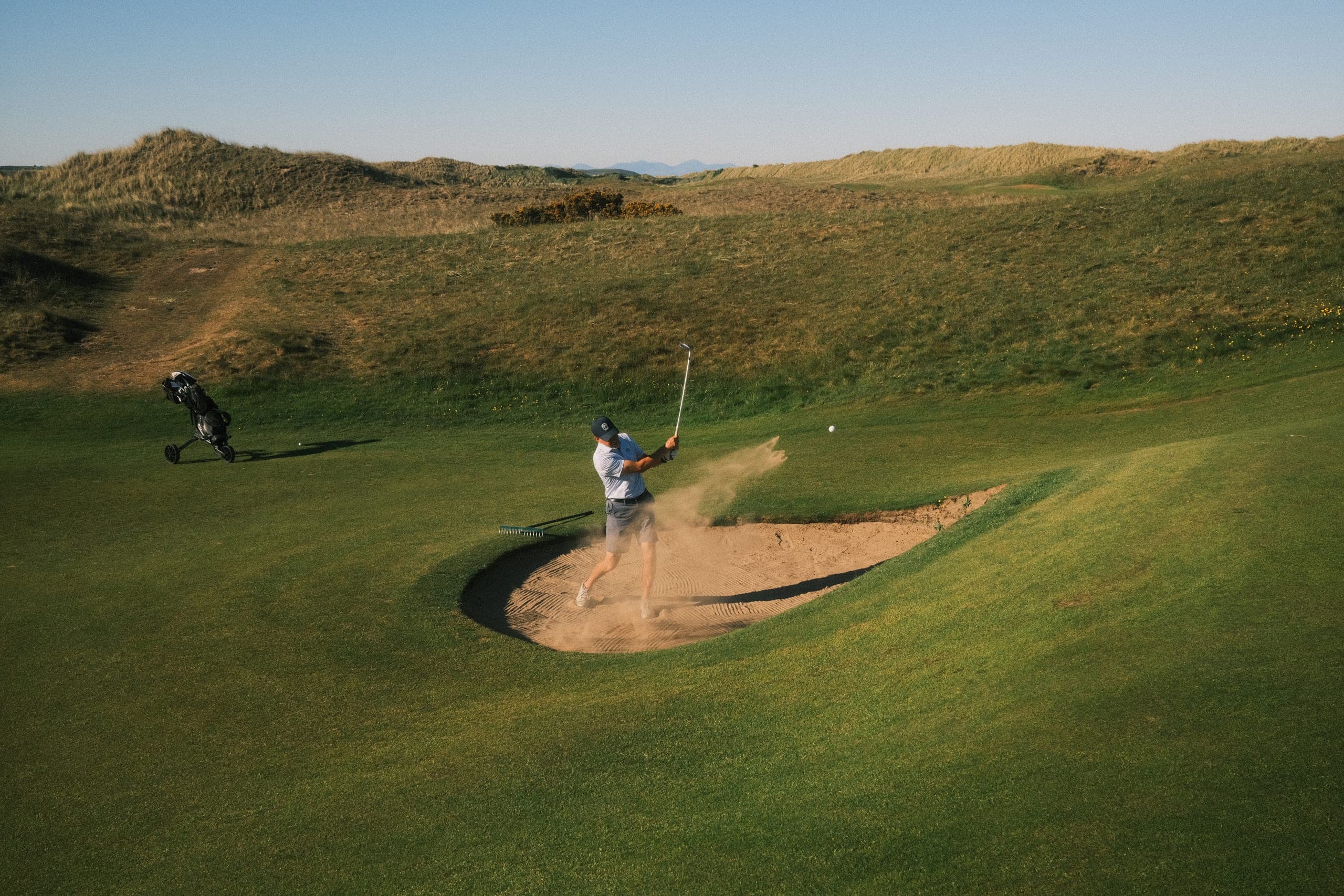 A bunker shot mid-spray among the dunes.