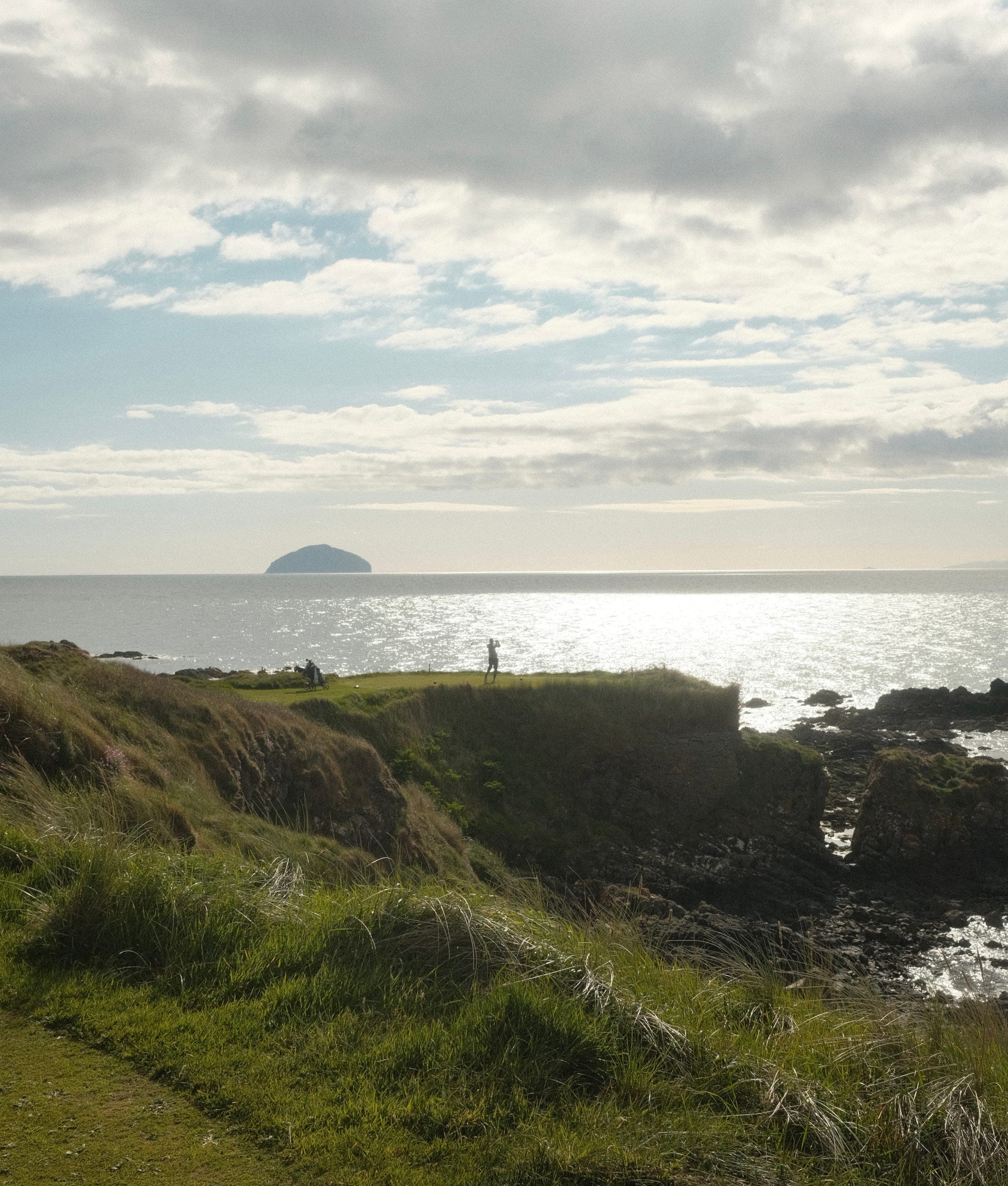 A tee shot from a rocky headland with Ailsa Craig on the horizon.