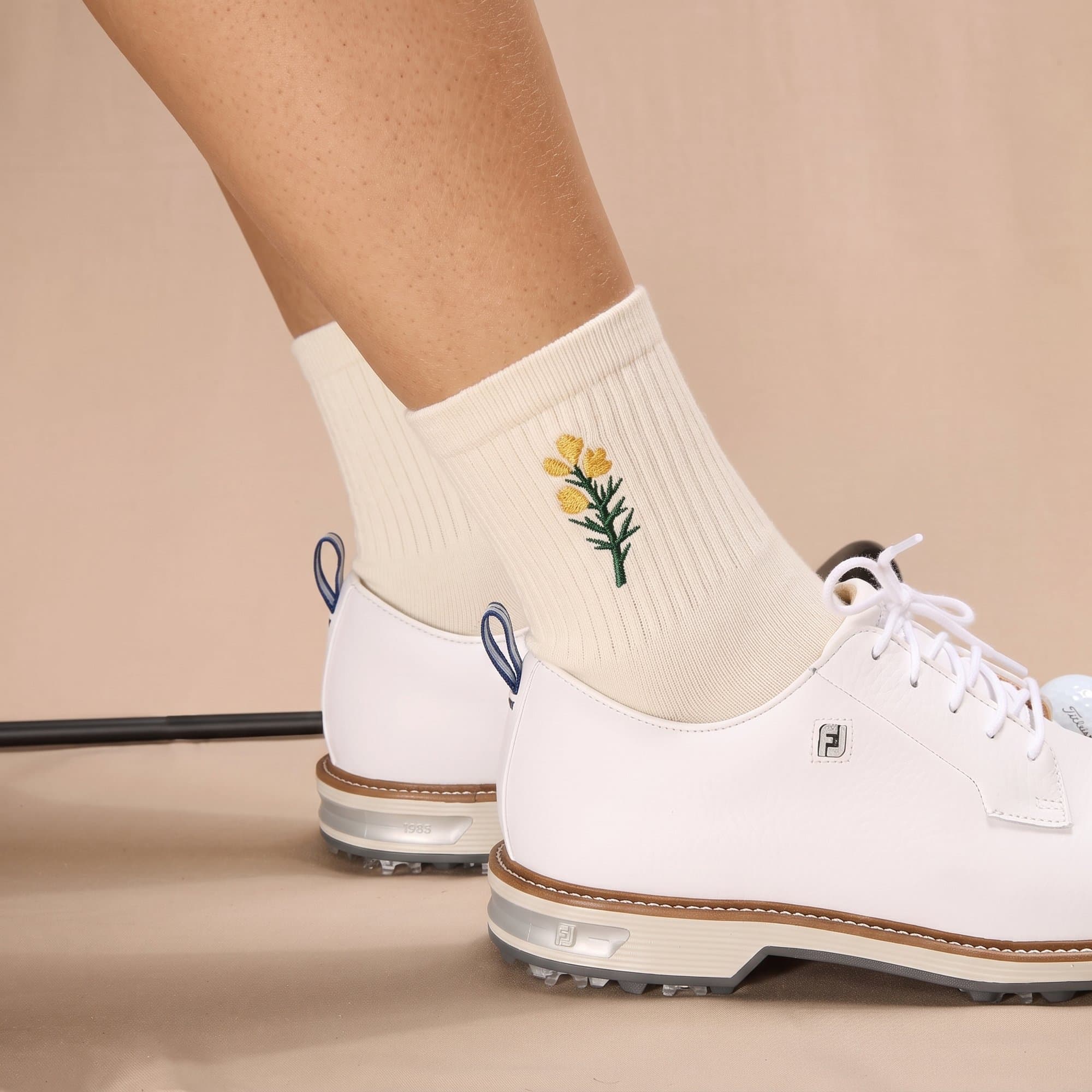 The socks worn with white golf shoes, the embroidered gorse at the cuff.